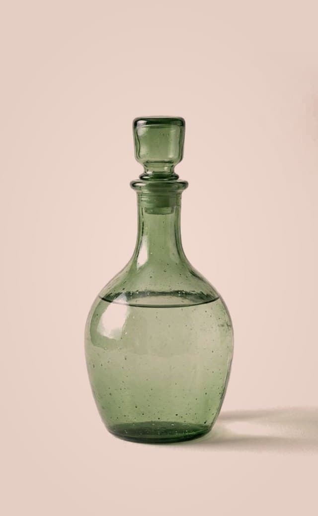 Carafe en verre soufflé vert sur fond rose